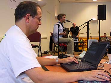Een harmonicaspeler, die behalve trekzak- ook nog eens computerverslaafd is, staart beteuterd naar zijn beeldschermpje. De directe verbinding met de Harmonicahoek wilde maar niet tot stand komen. Mark Söhngen op de achtergrond heeft duidelijk meer succes.