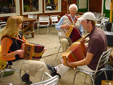 Volksmuziek wordt van generatie op generatie overgedragen. Hier gebeurt het letterlijk. De Terschellinger speelman Arie Doeksen jamt op een terras met twee jongere deelnemers aan de Soerense Harmonicadag.