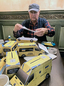 Eduard Bekker knutselt de Oekraense ambulances (met gleuf en QR-code) in elkaar bij de bar.